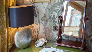 Une commode en bois surmontée d’un plateau en verre vert, une lampe noire, un miroir encadré et un coquillage décoratif.