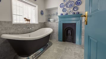 A bathroom with a freestanding bathtub, a marble-tiled floor, a blue door, and a wall decorated with blue and white ceramic plates.