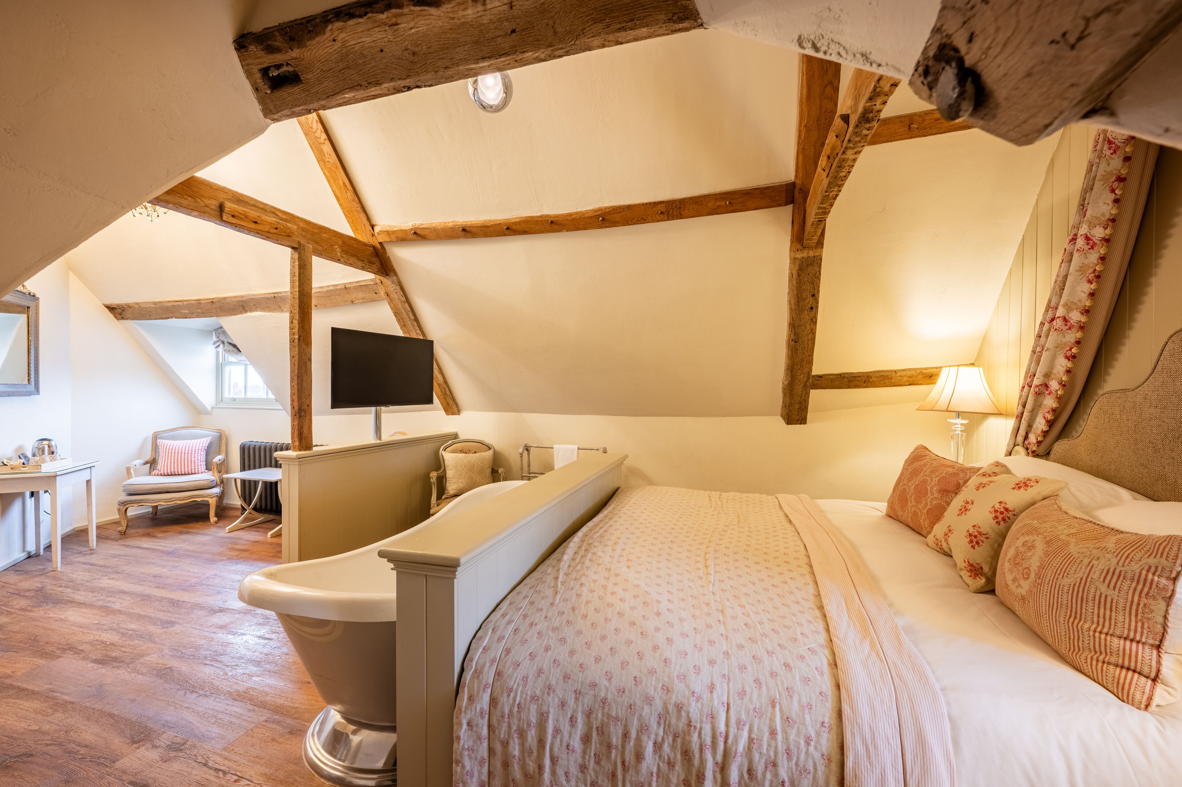 A bedroom with a large bed, a bathtub, a chair, and a desk.