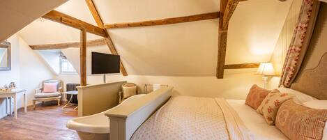 A bedroom with a large bed, a bathtub, a chair, and a desk.
