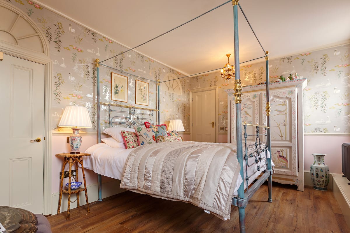 A four-poster bed with a canopy, a wooden floor, and floral wallpaper.