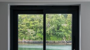 A window with a view of a calm body of water, a dock, and greenery. - The Shipwrights Arms (Helston)