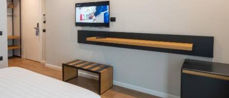 A modern bedroom with a bed, a TV mounted on the wall, a wooden bench, and a small black cabinet.