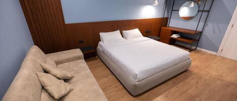Un dormitorio moderno con una cama grande, un sofá, una mesita de noche y un espejo.