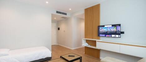 Una habitación de hotel moderna con una cama, una pequeña mesa, un sofá y un televisor montado en la pared.
