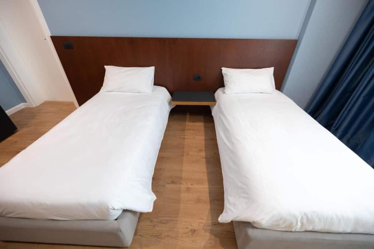 A room with two single beds, wooden headboard, white bedding, and a wooden floor.