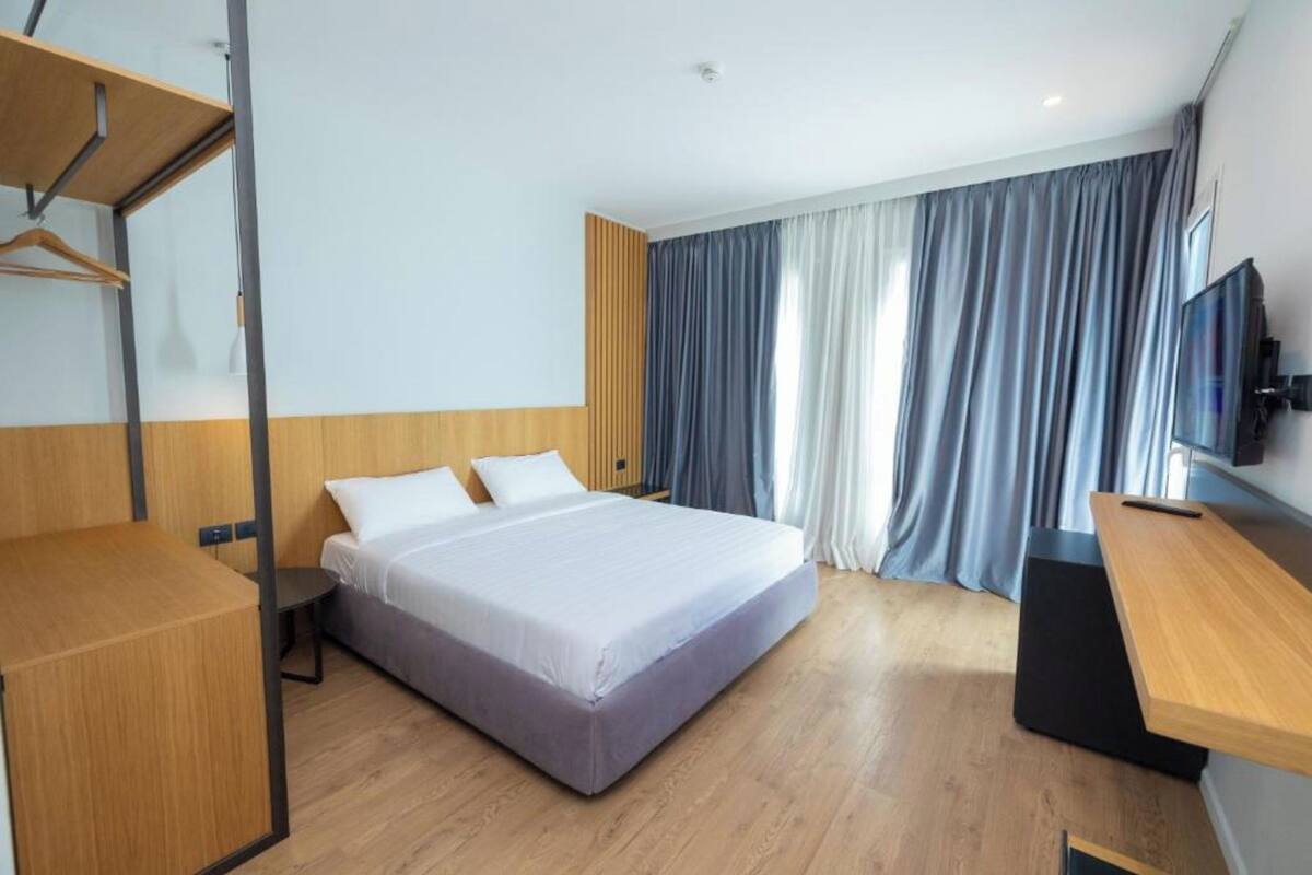 A modern hotel room with a bed, a desk, a TV, and a wardrobe.