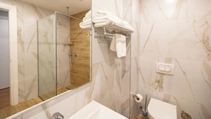 Un baño moderno con cabina de ducha de vidrio, un lavabo blanco y un perchero con toallas dobladas con pulcritud.