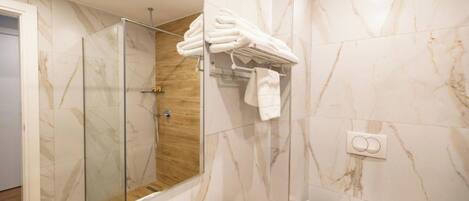 Un baño moderno con cabina de ducha de vidrio, un lavabo blanco y un perchero con toallas dobladas con pulcritud.