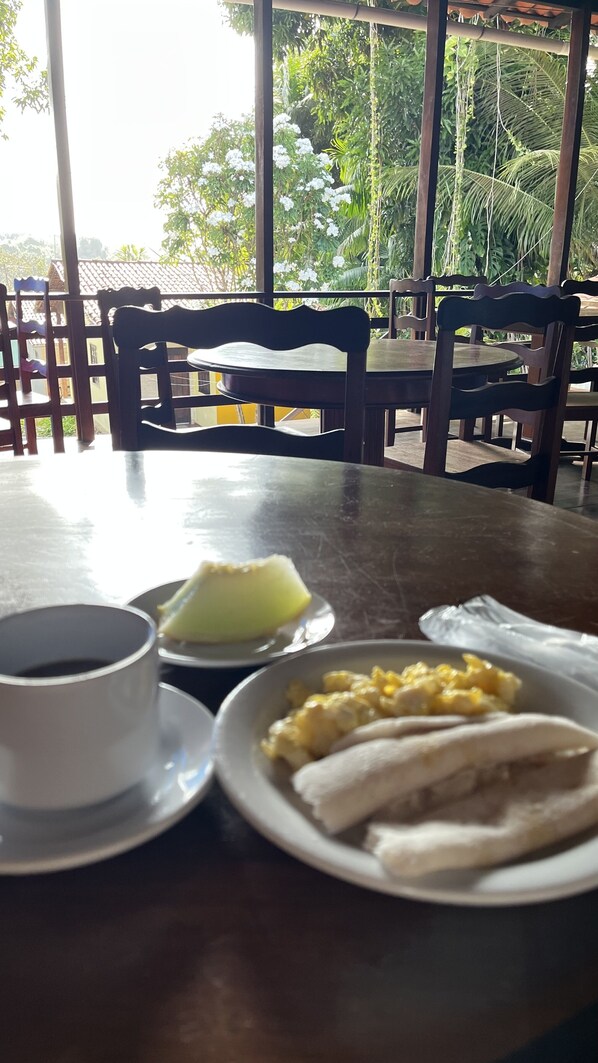 A table with a cup, a plate with food, and a glass of water. - Pousada La Maison Du Baron  (Alcantara)