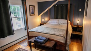 A bedroom with a four-poster bed, a bench with folded towels, a bedside table with a lamp, and a window with curtains. - Charming Dorset Cottage Retreat.  (Dorset)