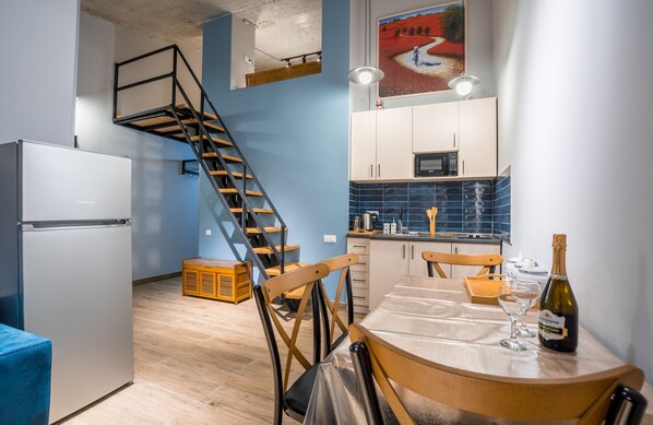 Una cocina moderna con una escalera de madera, un comedor con una mesa preparada para dos personas y una botella de champán sobre la mesa.