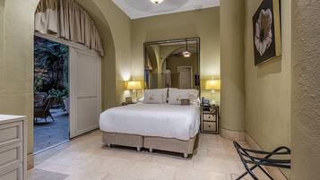 Un dormitorio con una cama grande, dos mesitas de noche con lámparas, un espejo y un arco que da a un espacio exterior.