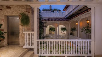 A covered outdoor area with a white railing, a door, and a staircase leading to an upper level.