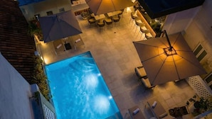 Piscina exterior con sillas de descanso y sombrillas, rodeada por una zona de patio con mesas y sillas.