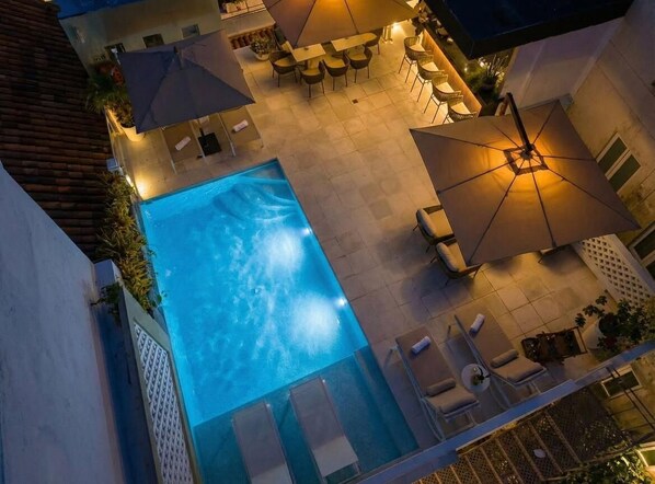 Piscina exterior con sillas de descanso y sombrillas, rodeada por una zona de patio con mesas y sillas.
