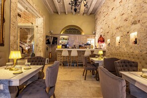 Un restaurante con pared de piedra, barra y diferentes distribuciones de mesas.