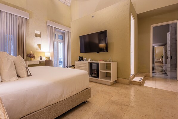 Une chambre d’hôtel dotée d’un grand lit, d’un téléviseur à écran plat fixé au mur, d’un minibar et d’un bureau avec une lampe.