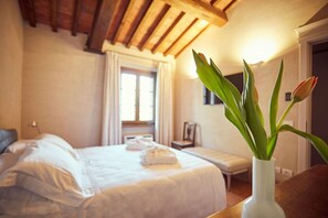 Hotellihuone, jossa on sänky, yöpöytä maljakko täynnä kukkia ja ikkuna, jossa on verhot.