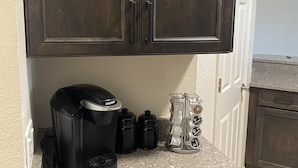 A kitchen with dark wooden cabinets, a granite countertop, a Keurig coffee maker, and a coffee pod dispenser. - Sunset Preserve on Lemon Bay Preserve  South Venice.  (Venice)