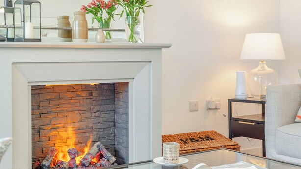 A modern living room with a stone fireplace, a glass coffee table with magazines, a lamp, and a wicker basket.