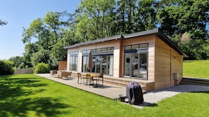 Een modern houten blokhut met een terras, grote ramen en tuinmeubilair.
