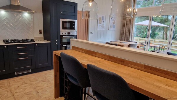 Een moderne keuken met een gasfornuis, zwarte kastjes en een houten eettafel met barstoelen.