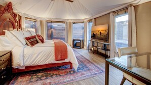 A spacious bedroom with a large bed, a glass table, and a view of the outdoors. - The Covey an African Tent Retreat Bluebird House (Garland County)