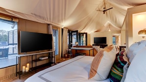 A spacious tented room with a large bed, a flat-screen TV, a desk, and a chair.