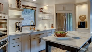 A modern kitchen with white cabinetry, a stainless steel refrigerator, a coffee maker, and a bowl of salad on the counter.