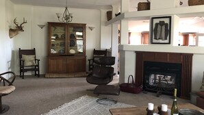 A cozy living room with a fireplace, a wooden cabinet with glass doors, and a chandelier. - Secluded & Spacious River Retreat With A View  (Roosevelt)