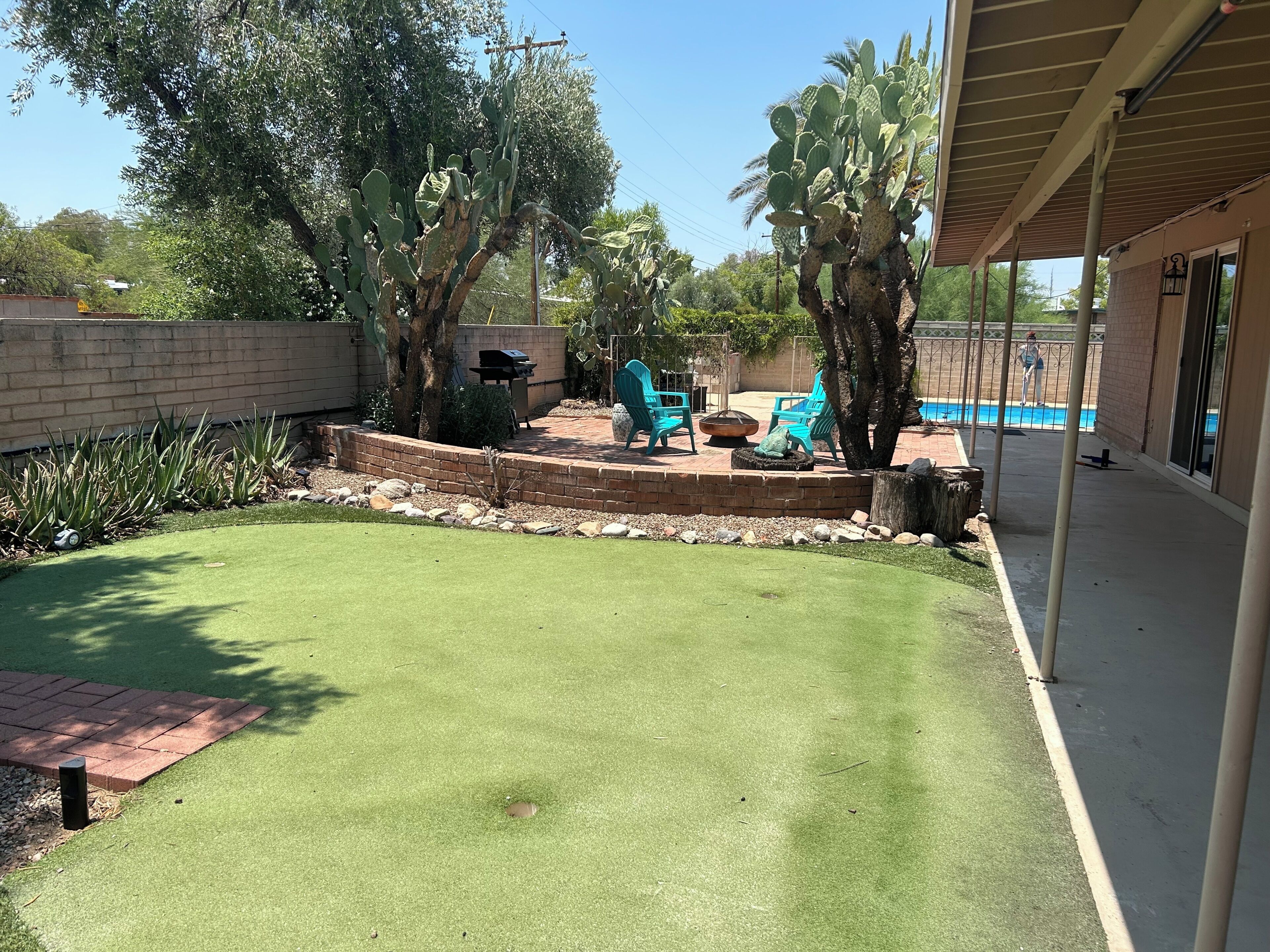 Ein Garten mit Terrasse, Sitzgelegenheiten im Freien, einem Pool und einer Kakteenpflanze.