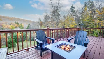 A wooden deck with two Adirondack chairs and a fire pit.