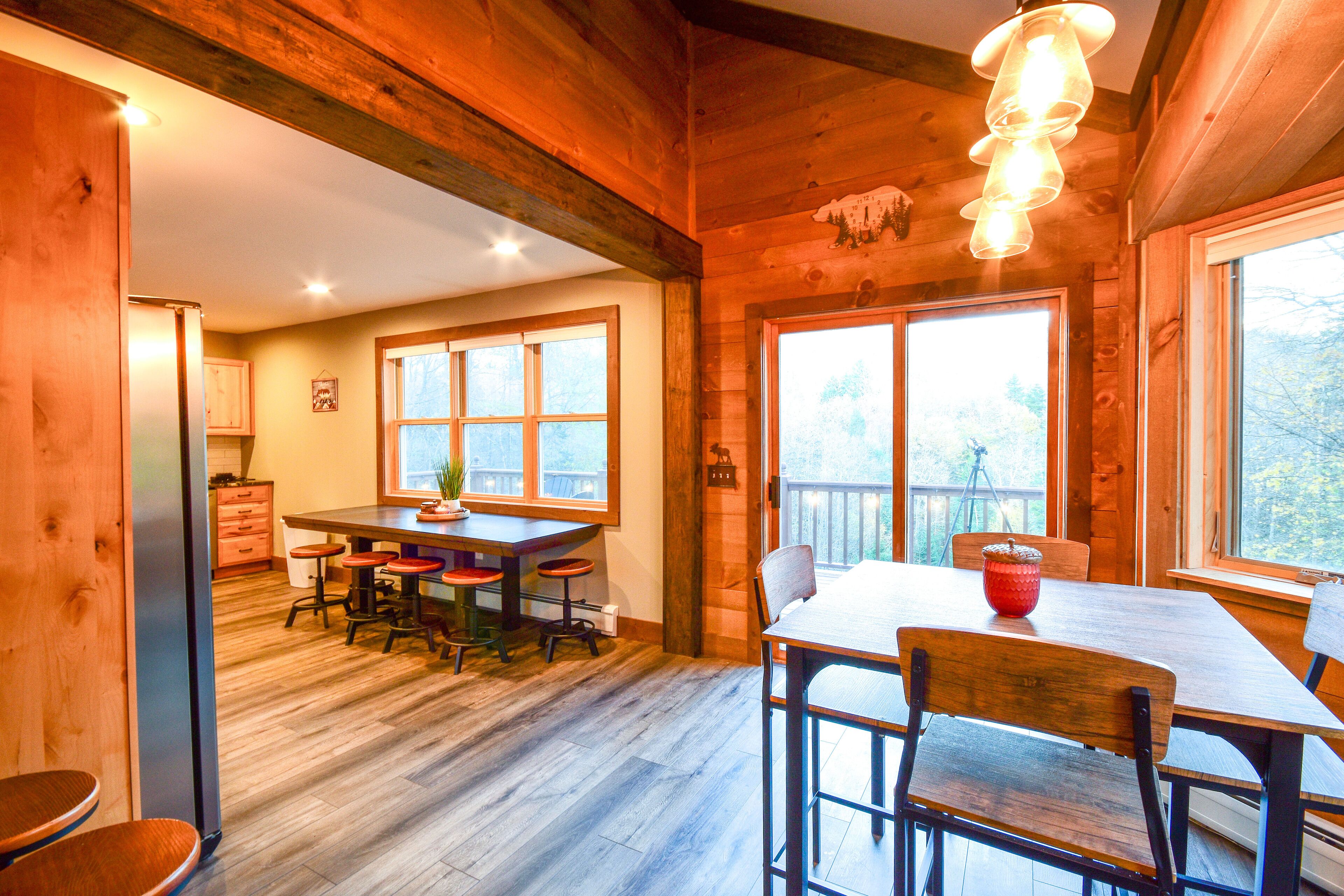 A wooden interior with a dining area, kitchen, and large windows.