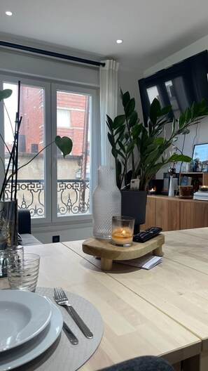 Uma área de refeições com uma mesa posta para dois, uma vela, um controle remoto e um vaso com planta.