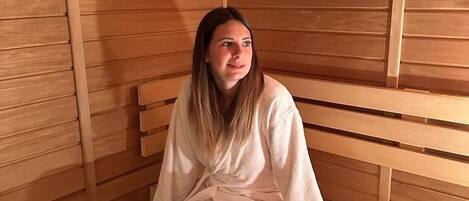 A sauna with wooden benches and a person sitting on one.