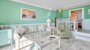 Un salon avec un canapé à rayures, un fauteuil vert, une table basse blanche et un tableau accroché au mur.