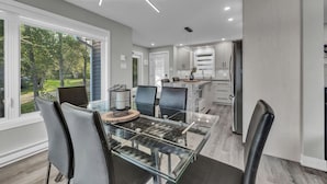A modern kitchen with a dining area, large windows, and a view of the outdoors. - The family cottage at Lac Sainte-Marie (Lac-Sainte-Marie)