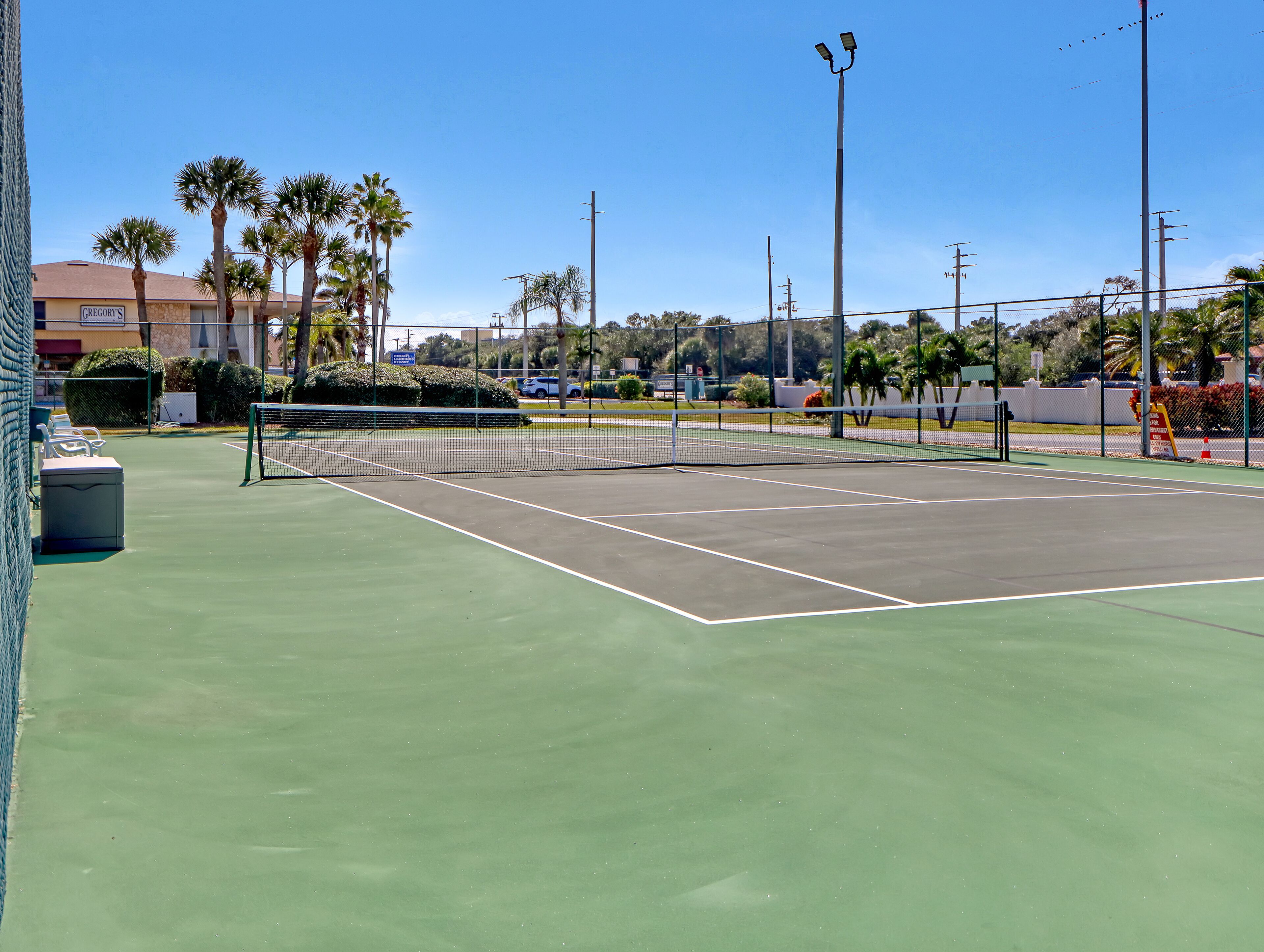 A tennis court with a net, surrounded by palm trees and a fence.