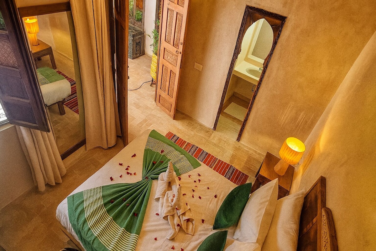 Habitación de hotel con cama, espejo, lámpara y vistas al exterior.