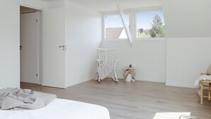 Une chambre avec une grande fenêtre, un fauteuil à bascule blanc, une petite table d’appoint et un lit.