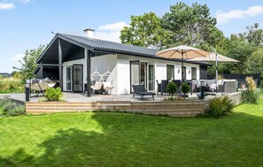 Una casa moderna con un porche cubierto, mobiliario de exterior y un jardín.