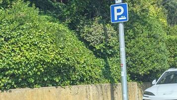 Una señal de estacionamiento con fondo azul y letras blancas, una barrera de concreto y un vehículo en la carretera.