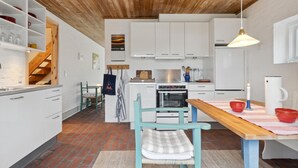 Una cucina moderna con mobili bianchi, soffitto in legno e zona pranzo con tavolo e sedie.
