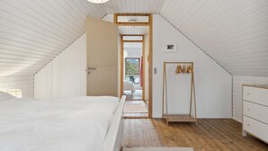 Camera con soffitto spiovente, un letto, una panca in legno, un armadio e una finestra vista verde.