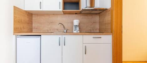 A compact kitchen with white cabinets, a built-in dishwasher, a coffee maker, and a stainless steel range hood.