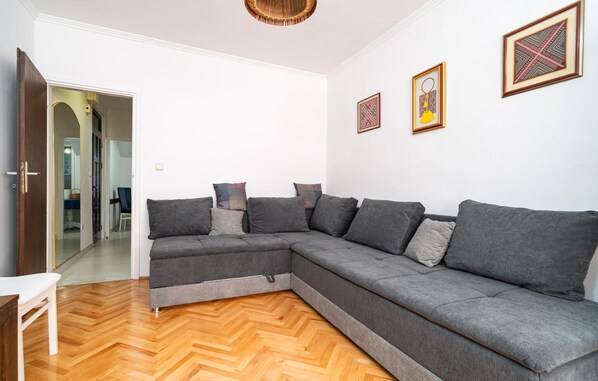 Een moderne woonkamer met een grijze modulaire bank, houten parketvloer en twee ingelijste kunstwerken aan de muur.