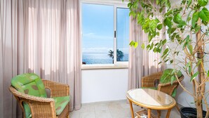 Un balcón con vistas al mar, muebles de mimbre y una planta en maceta.