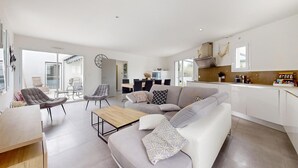 En moderne stue med en grå sofa, et træbord og et spiseområde med et køkken i baggrunden.