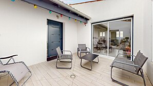 En overdækket terrasse med en blå dør, to metalstole, et lille bord og et tøjstativ.